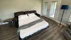 Een slaapkamer met een bed, nachtkastje, lamp en een schuifdeur naar een balkon.