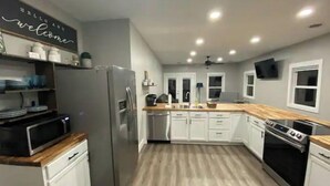 Een moderne keuken met witte kasten, een roestvrijstalen koelkast, een magnetron, een vaatwasser en een houten aanrecht.