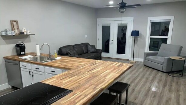 Een moderne keuken met een houten aanrechtblad, inbouwapparatuur en een zithoek met een grijze bank en een bijzettafeltje.
