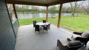 Een overdekt terras met een tafel en stoelen, met uitzicht op een rivier.