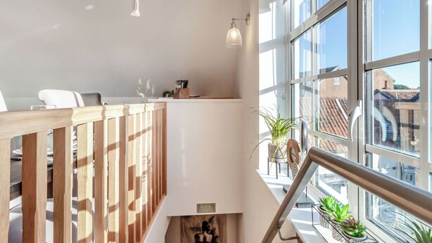 Un intérieur moderne avec une balustrade en bois, un coin repas et de grandes fenêtres offrant une vue sur la ville.