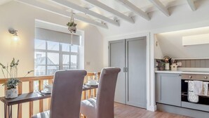 Un coin repas comprenant une table en bois, deux chaises, une fenêtre donnant sur un paysage agréable et une cuisine équipée d’une cuisinière et de placards.