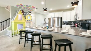 Une cuisine moderne dotée d’un îlot central, d’appareils électroménagers en acier inoxydable et d’une décoration ludique représentant une maison de jeu jaune.