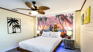 Une chambre à coucher avec un lit, un ventilateur de plafond, une table de chevet, une fresque murale et un plancher en bois.