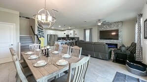 Une cuisine moderne équipée d’appareils électroménagers en acier inoxydable, un coin repas avec des tables et des chaises en bois, un salon doté d’une grande télévision et de sièges confortables, et un escalier menant à un autre niveau.