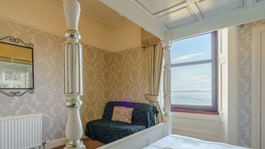 A four-poster bed with a view of the sea, a patterned wall, and a radiator. - The Old Nunnery - UK7122 (Skelmorlie, near Largs)