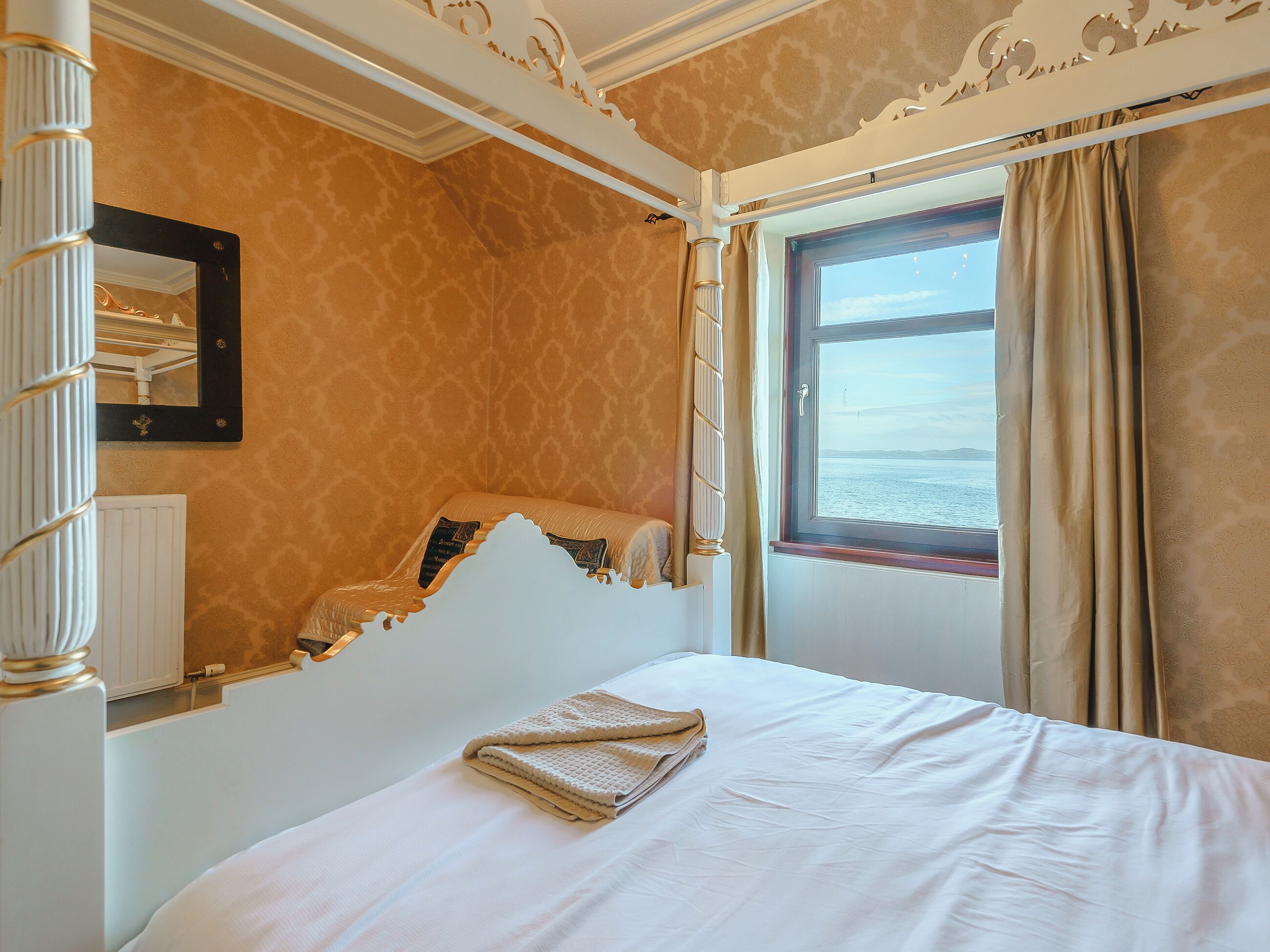 A room with a bed, a window with curtains, a mirror, and a radiator.