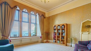 A room with a large bay window, a wooden bookcase, a blue armchair, and a patterned sofa. - The Old Nunnery - UK7122 (Skelmorlie, near Largs)