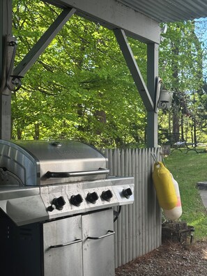 A barbecue grill with a metal hood, a control panel with knobs, and a yellow hanging bag. - Vienna's Place (Freeport)
