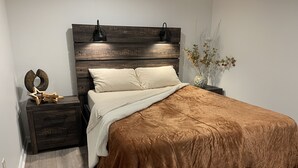 A bedroom with a wooden headboard, two bedside lamps, a decorative star, a vase with branches, and a brown bedspread.