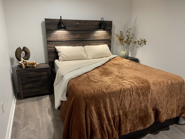 Slaapkamer met een houten hoofdbord, twee bedlampen, een decoratieve ster, een vaas met takken en een bruine sprei.