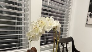 A dining table with a vase of white orchids, a wooden sculpture, a glass dish with cookies, and a magazine.