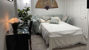 Een keurig opgemaakt slaapkamer met een bed, nachtkastje, lamp en een decoratieve ventilator.