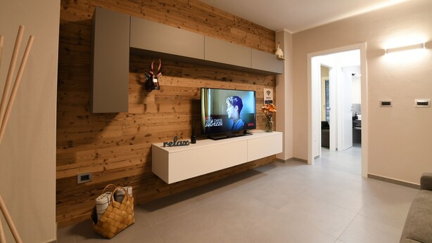Un salon moderne avec un panneau mural en bois, un téléviseur à écran plat, un meuble de rangement blanc et un sac en fibres naturelles posé sur le sol.