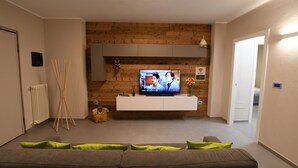 Un salon moderne doté d’un téléviseur à écran plat, d’un mur d’accent en bois, d’une console blanche et d’un canapé gris agrémenté de coussins verts.