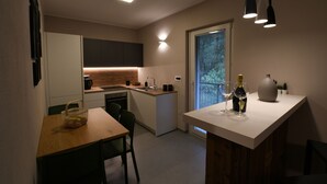 Une cuisine moderne avec une table à manger en bois, un four encastré et un petit îlot central sur lequel se trouvent une bouteille de vin et des verres.