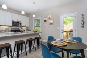 A modern kitchen with white cabinets, a microwave, and a stove. There are bar stools and a dining table with blue chairs.