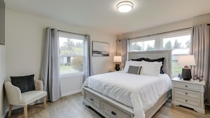 A bedroom with a large bed, bedside tables, a chair, and a window with curtains. - Spacious Updated Place at Harbor Home Base (Oak Harbor)
