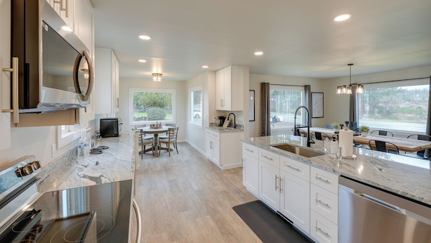 A modern kitchen with white cabinetry, stainless steel appliances, and a large island with a sink. - Spacious Updated Place at Harbor Home Base (Oak Harbor)