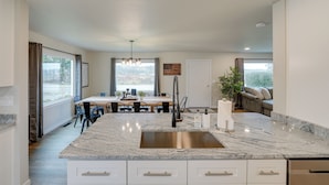 A modern kitchen with a granite countertop, stainless steel sink, and a dining area with a table and chairs. - Spacious Updated Place at Harbor Home Base (Oak Harbor)