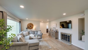 A spacious living room with a grey sofa, a round coffee table, and a fireplace. - Spacious Updated Place at Harbor Home Base (Oak Harbor)