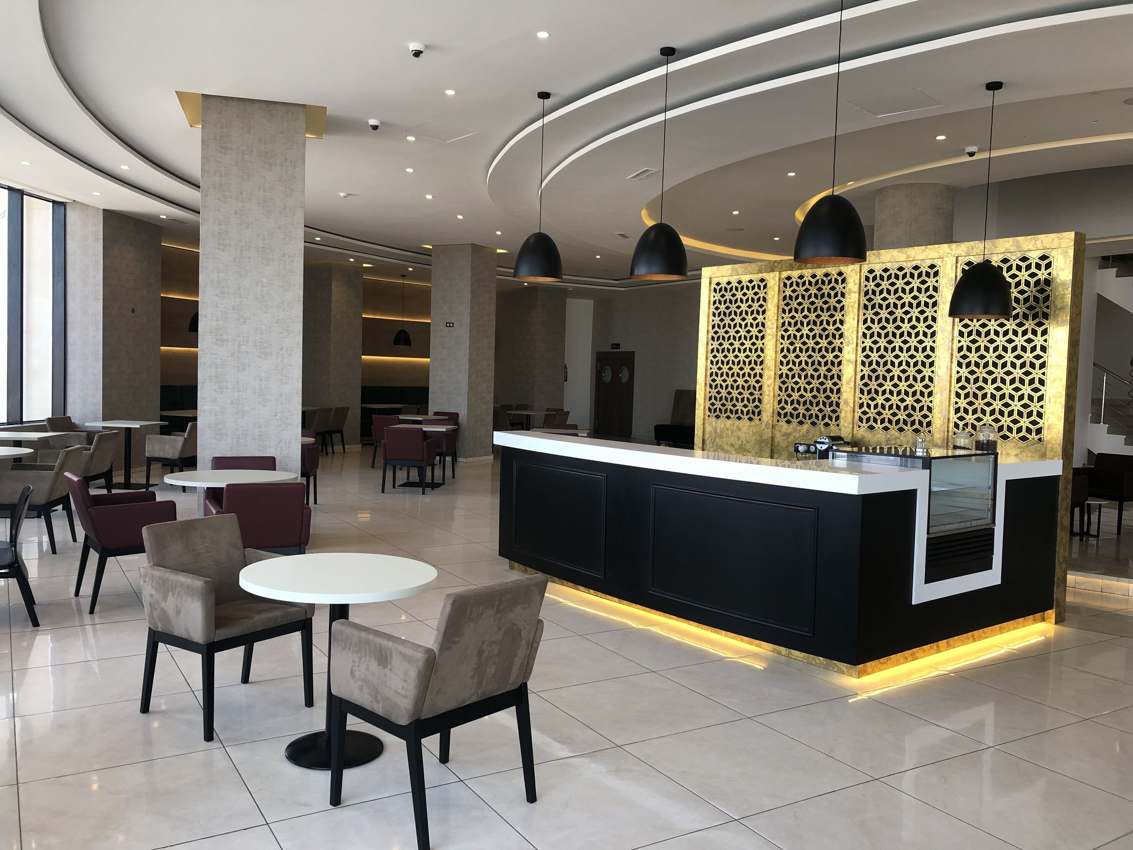 A modern hotel lobby with a central reception desk, seating area, and a decorative partition with geometric patterns.