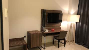 Habitación de hotel con un escritorio de madera, una silla, un televisor montado en la pared, una lámpara de pie y un pequeño banco.