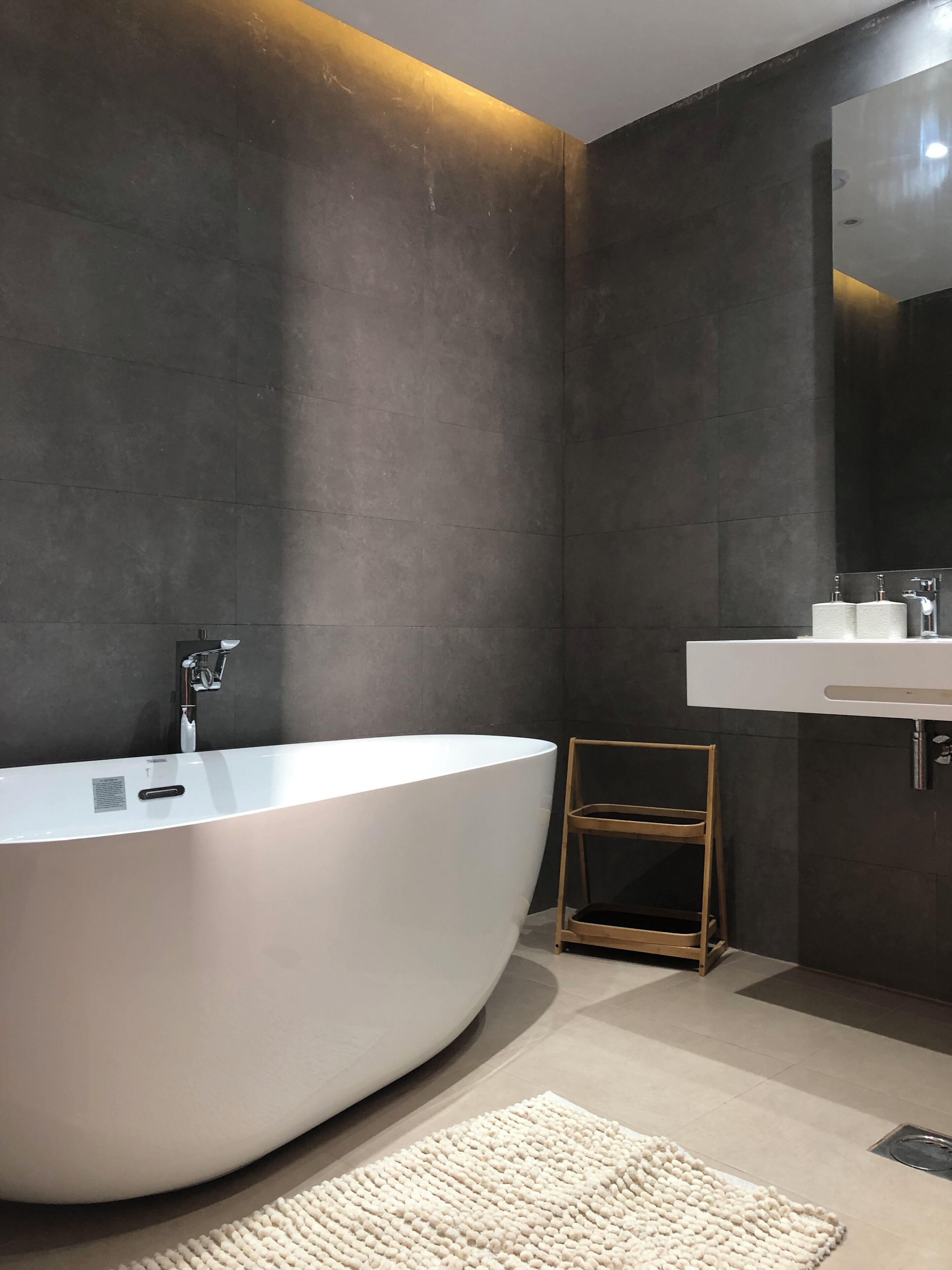 A modern bathroom with a freestanding bathtub, a wooden stool, and a white sink with a mirror above it.