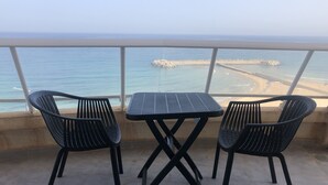 En balkon med to sorte metalstole og et bord, der ud til en strand med en moler.