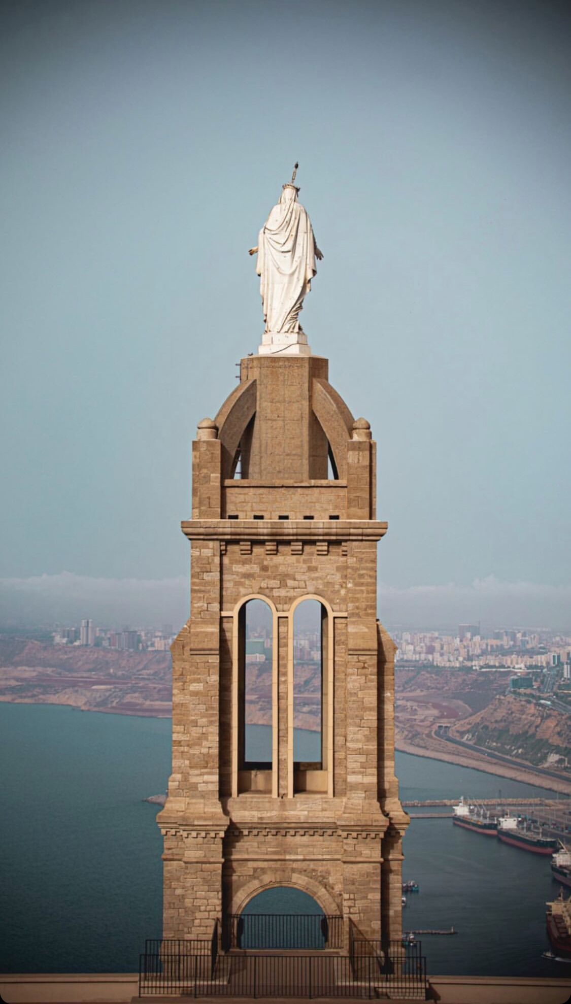 A tall, stone monument with a statue on top, featuring arched windows and a balcony.