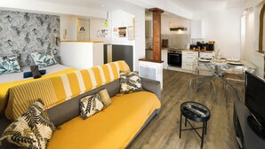 A modern apartment with a large bed, a sofa, a dining table, and a kitchen area.