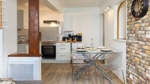 A compact kitchen with white cabinets, a wooden column, and a glass dining table with chairs.