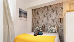 A bedroom with a bed, a tropical wallpaper headboard, a dreamcatcher, and a framed picture on the wall.