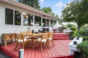 A wooden deck with a table and chairs, a small outdoor kitchen, and a view of a forested area. - Historic River Front Farmhouse Near Wineries-Private waterfront! Winery tour! (Prosser)