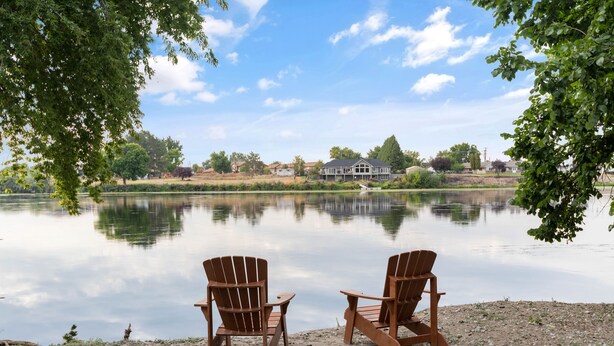 Dos sillas Adirondack mirando un lago tranquilo con una casa al fondo.
