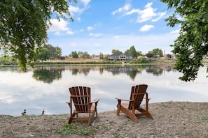 Dos sillas Adirondack mirando un lago tranquilo con una casa al fondo.