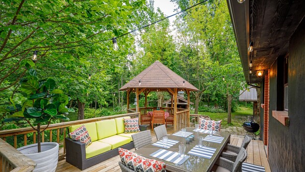 Une terrasse extérieure avec un gazebo en bois, une table à manger avec des chaises, un canapé et un barbecue.
