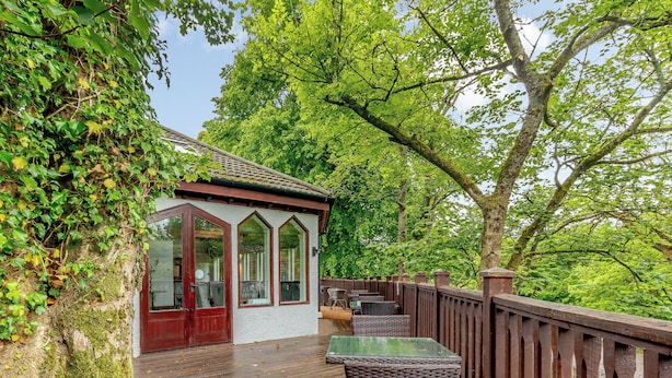 Eine Holzterrasse mit Glasveranda, umgeben von üppigem Grün und Bäumen.