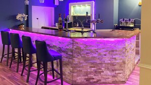 Eine Bar mit einer Theke aus Steinoptik, Barhocker und einer Neonleuchte.