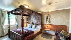 Ein Bett mit Himmelbett, ein Holzkopfstück, ein Nachttisch mit Lampe und ein Spiegel an der Wand.