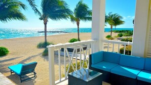 Een terras aan het strand met een rieten bank en een lounge stoel, met uitzicht op de oceaan.