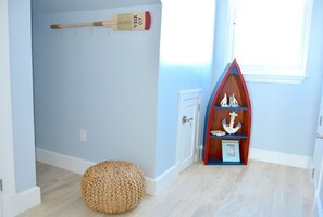 Ein Zimmer mit hellblauen Wänden, Holzboden, einem kleinen runden Sitzsack, einem Holzregal mit nautischen Dekorationen und einer Tür mit weißem Rahmen.