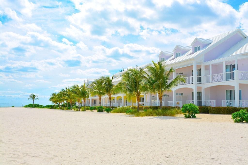 A beachfront hotel with multiple-story buildings, palm trees, and a sandy beach.