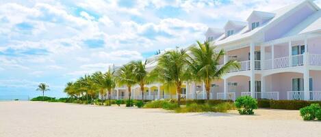 A beachfront hotel with multiple-story buildings, palm trees, and a sandy beach.