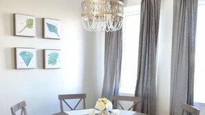 Een eetruimte met een ronde tafel, zes houten stoelen, een kroonluchter en kunstwerken in lijsten aan de muur.