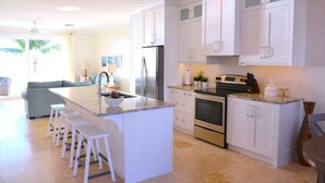 Een moderne keuken met witte kasten, een centraal eiland met krukken, roestvrijstalen apparatuur en uitzicht op de woonkamer.
