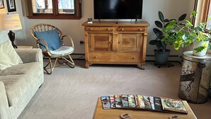 Un salon avec un canapé, une table basse sur laquelle sont posés des magazines, un téléviseur sur un meuble en bois, un fauteuil en osier et une plante en pot.