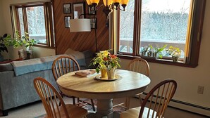 Un coin repas avec une table ronde, quatre chaises, un lustre et une vue sur un paysage enneigé grâce à de grandes fenêtres.