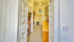 A narrow hallway leading to a kitchen with a washing machine, a wooden counter, and a small window. - FORTUNE GUESTHOUSE (Lisbon)
