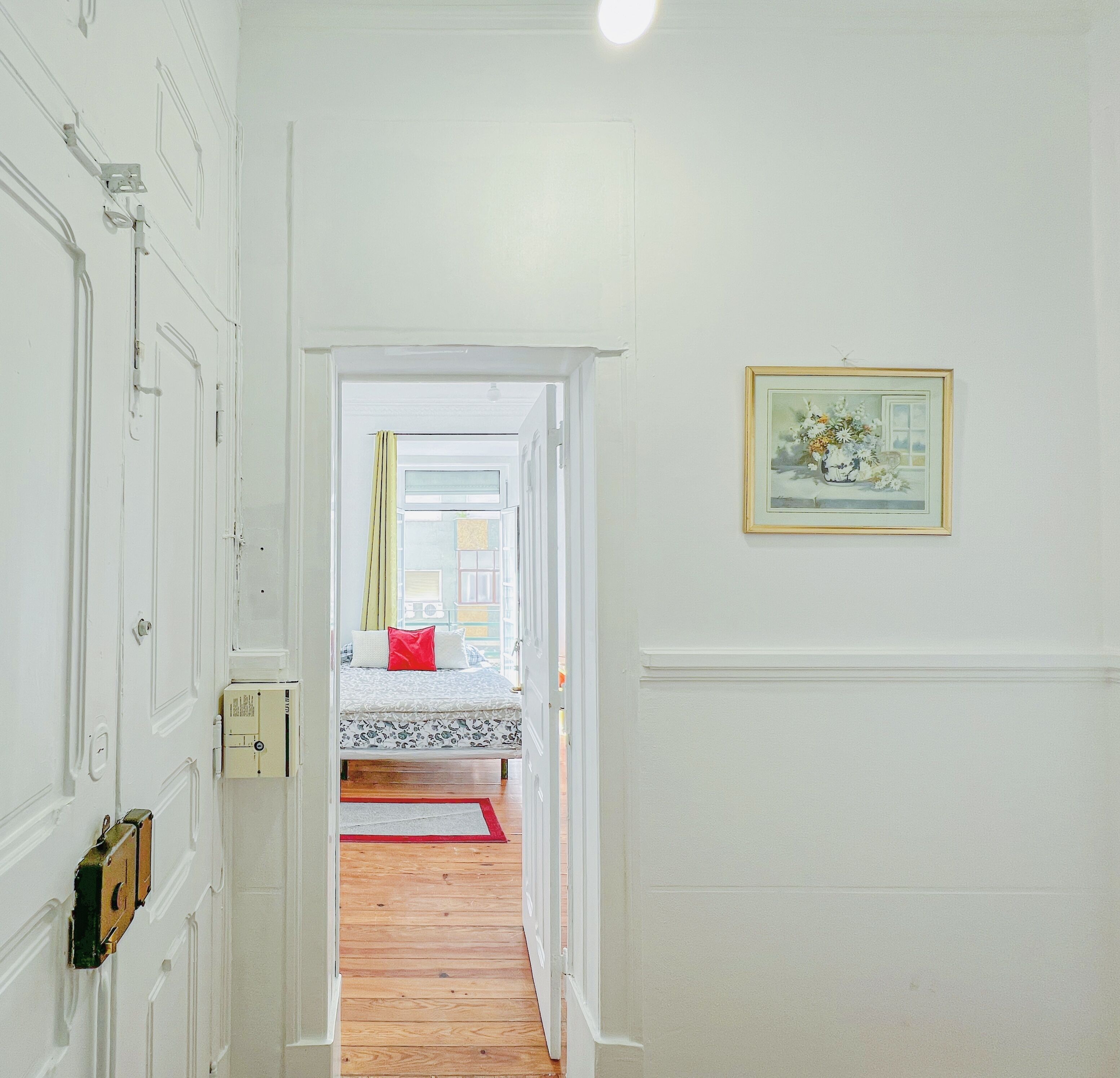 A hallway leading to a bedroom with a bed, a door, and a framed picture on the wall.
